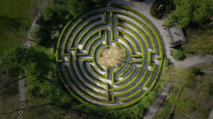 Vista aérea de un gran laberinto circular hecho de setos verdes ubicado en un parque o jardín que representa la situación actual del propietario de PYME que busca mejorar su rentabilidad.