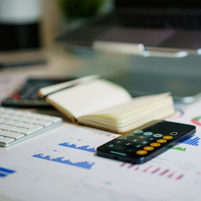 Un escritorio de trabajo con gráficas financieras, calculadora y cuaderno en blanco.