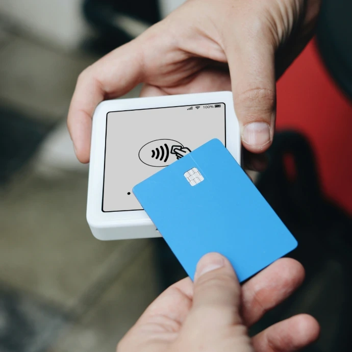 La mano de una persona acercando una tarjeta bancaria azul a un datáfono blanco para realizar un pago sin contacto.